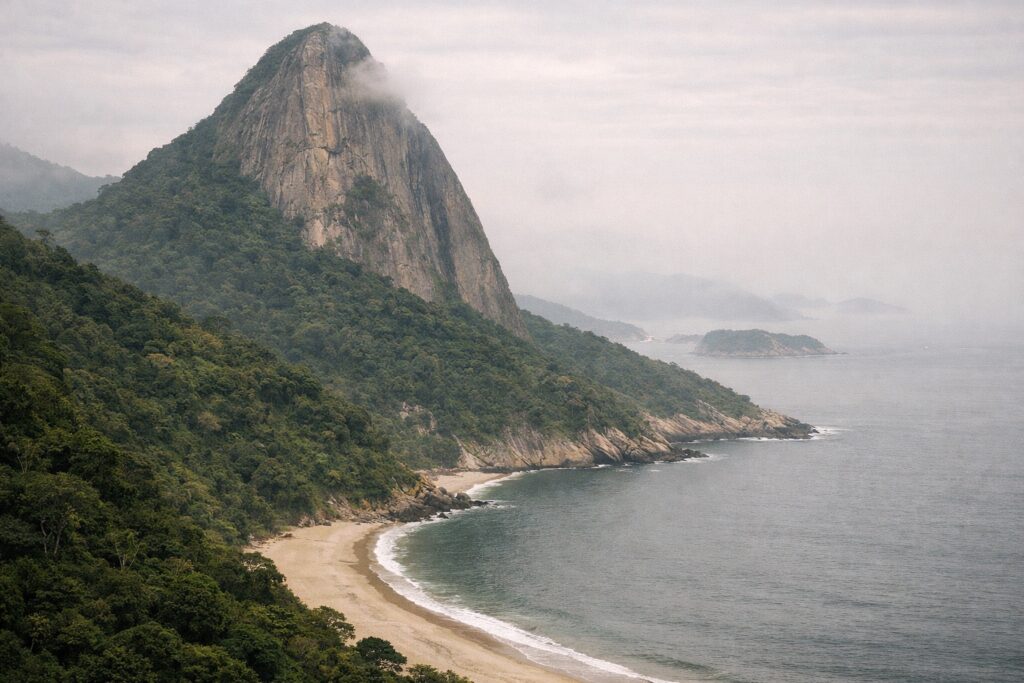 Pico de granito coberto de floresta sobre uma baía com praia em arco e bruma húmida
